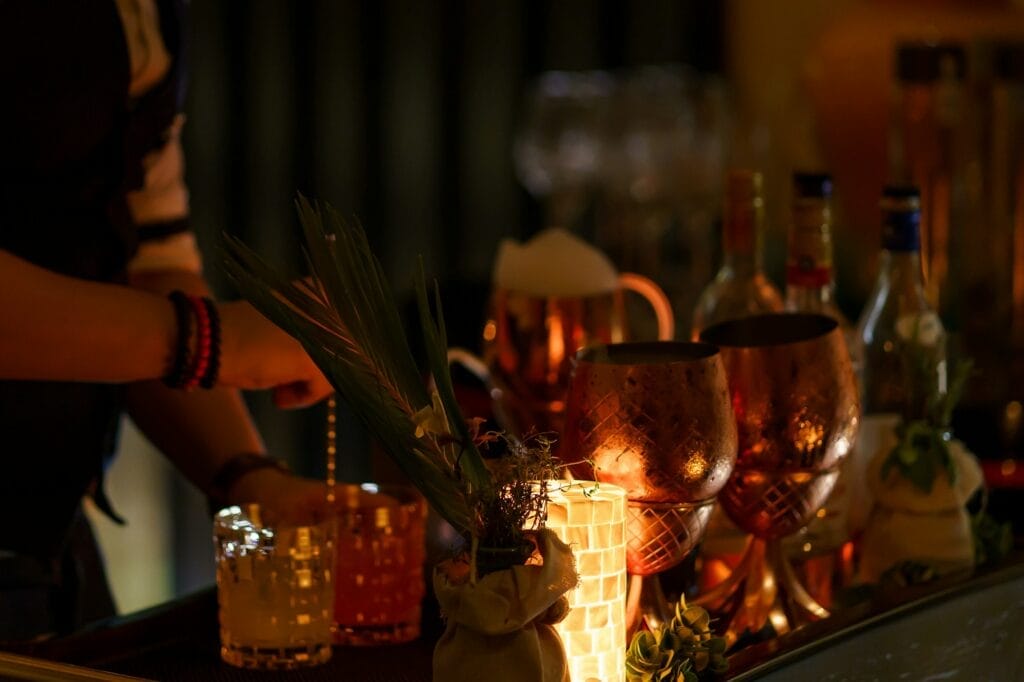 Barman skillfully preparing a cocktail on a moving bar tray, featuring elegant glasses and colorful garnishes.