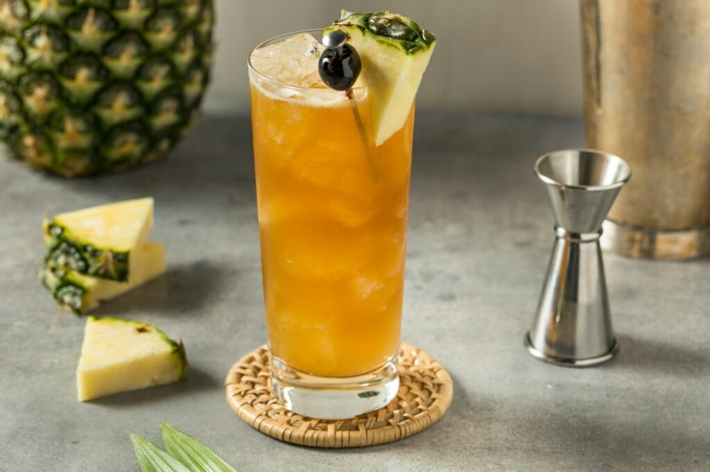 A vibrant Bahama Mama cocktail garnished with a slice of orange and a cherry, served in a tall glass.