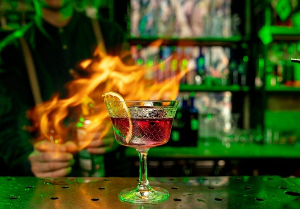 Close up of a vibrant alcoholic cocktail illuminated by multicolored neon lights, with flames enhancing its visual appeal.